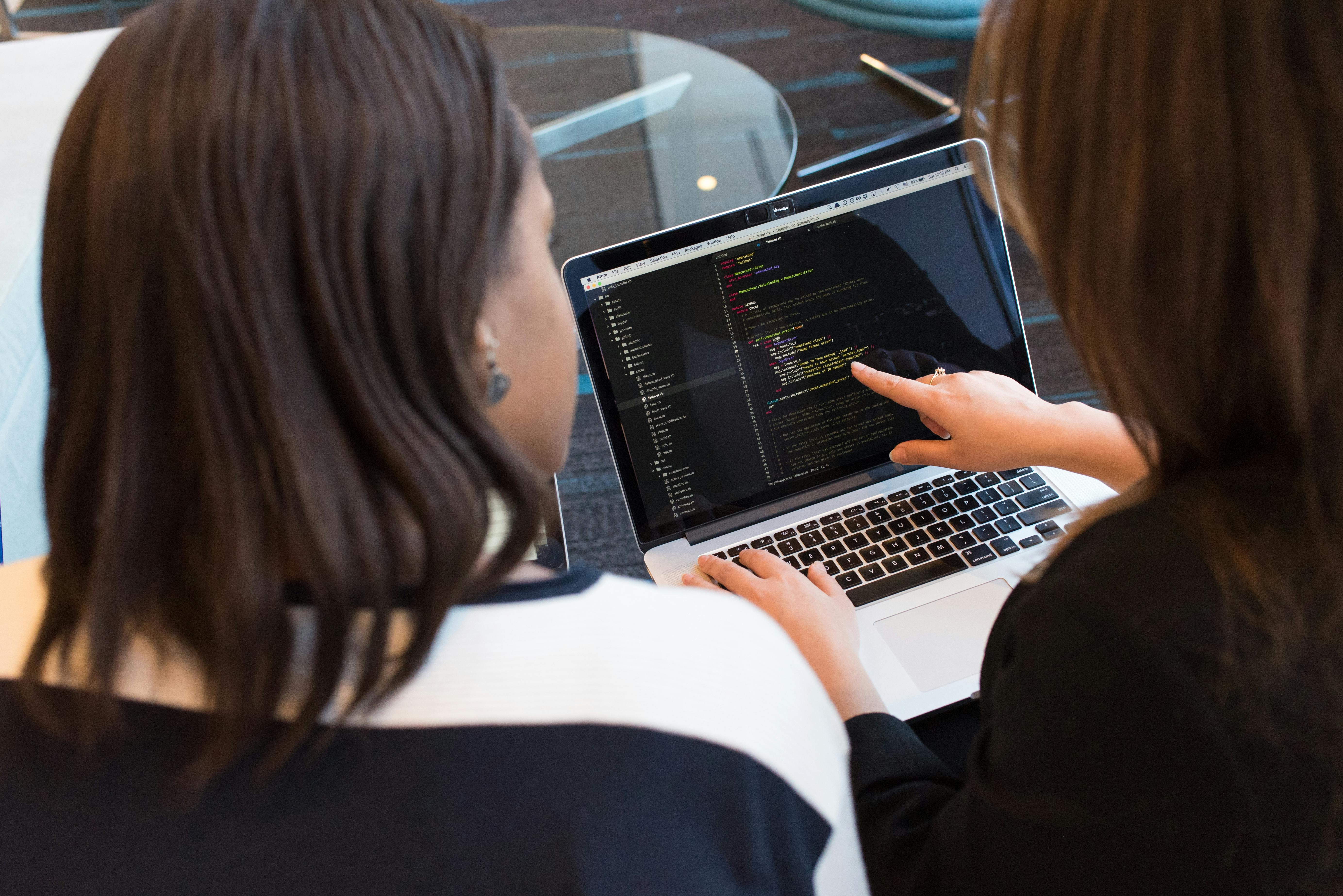 two Women sitting in front of a laptop reviewing code.