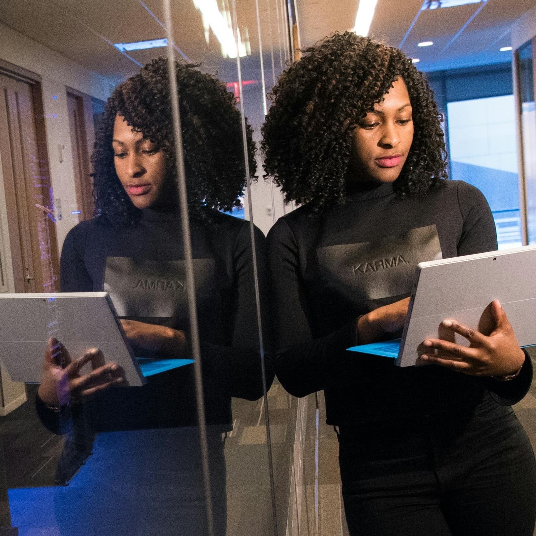 Person leaning against a glass window, holding an open laptop.